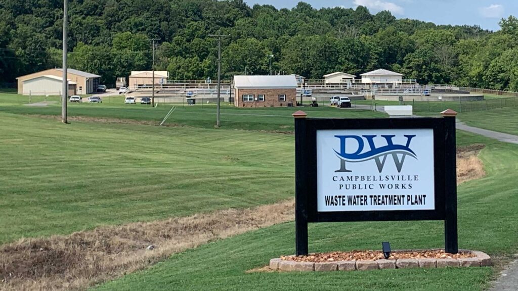 Sign for Campbellsville Public Works Wastewater Treatment Plant with facility buildings and treatment basins in the background.